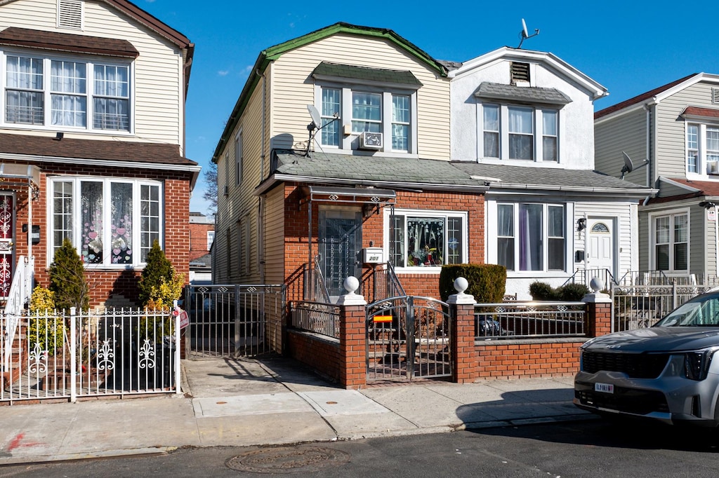 view of front facade featuring a gate, brick siding, a fenced front yard, and a shingled roof