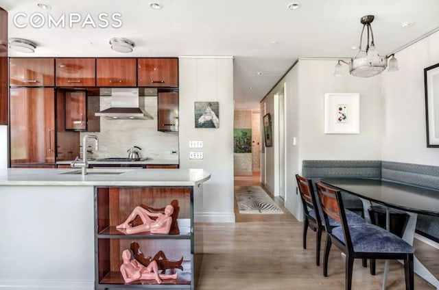 kitchen with tasteful backsplash, light countertops, light wood-style floors, a sink, and wall chimney range hood