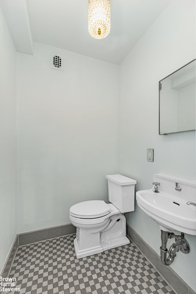 bathroom featuring toilet, a sink, visible vents, baseboards, and an inviting chandelier