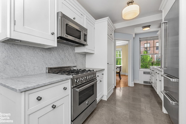 kitchen with high quality appliances, white cabinetry, light stone countertops, tasteful backsplash, and radiator heating unit