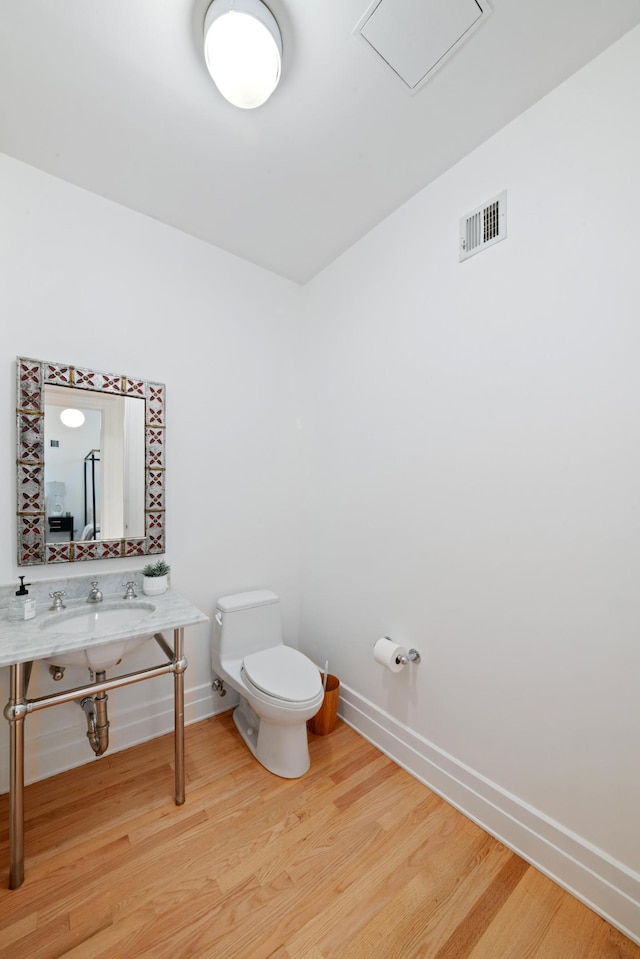 half bathroom with a sink, toilet, baseboards, wood finished floors, and visible vents