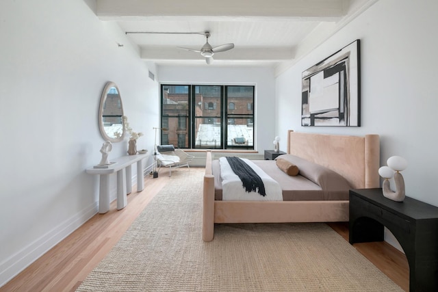 bedroom featuring a ceiling fan, beamed ceiling, baseboards, and wood finished floors