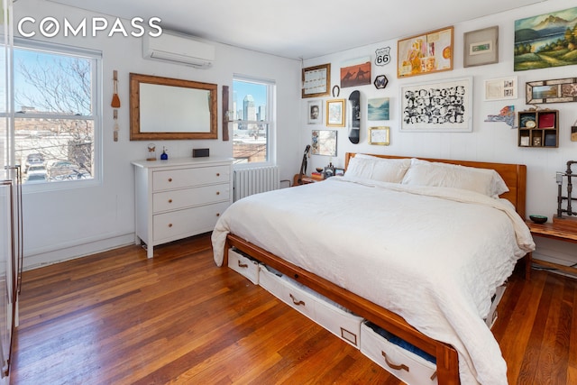 bedroom with a wall unit AC, radiator heating unit, and wood finished floors