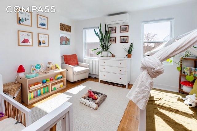 rec room with a wall mounted AC, hardwood / wood-style flooring, and radiator