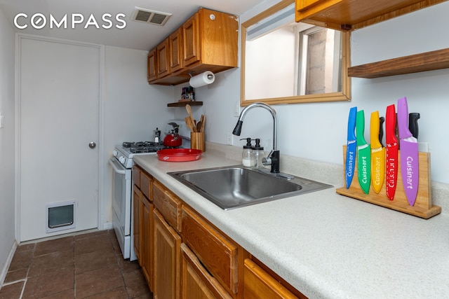 kitchen featuring open shelves, white gas range, light countertops, visible vents, and a sink