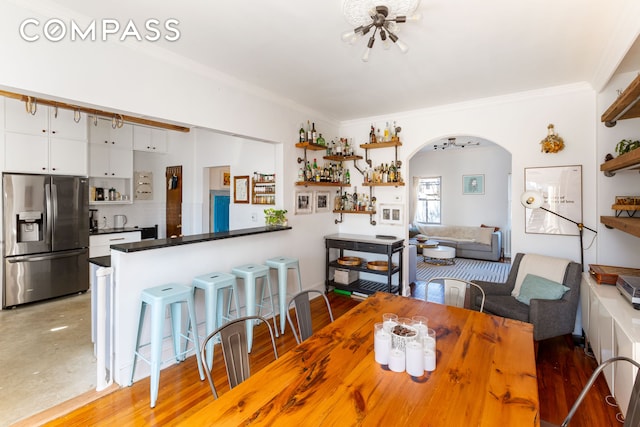 dining area with arched walkways, light wood-type flooring, a chandelier, and crown molding