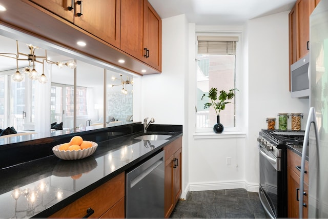 kitchen with a sink, stainless steel appliances, dark stone countertops, and brown cabinetry