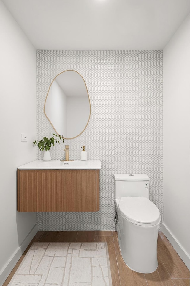 bathroom featuring toilet, vanity, wood finished floors, baseboards, and wallpapered walls