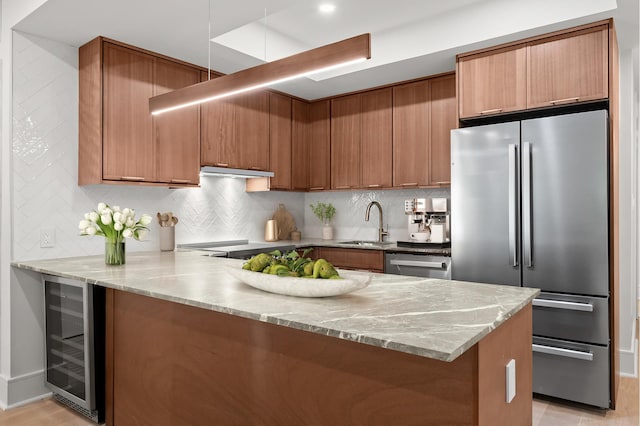 kitchen with beverage cooler, appliances with stainless steel finishes, brown cabinets, a peninsula, and a sink