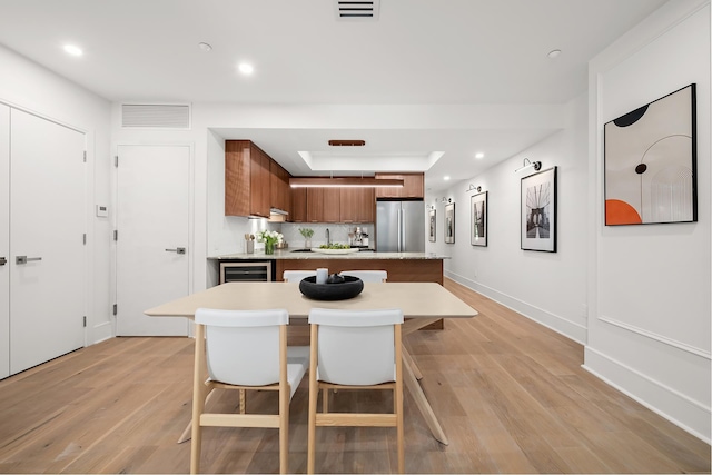 kitchen featuring light countertops, visible vents, light wood-style flooring, brown cabinetry, and stainless steel refrigerator