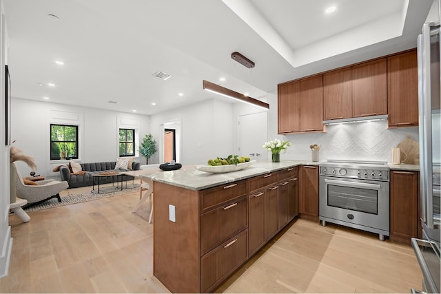 kitchen with brown cabinetry, light wood-type flooring, high end stove, a peninsula, and exhaust hood