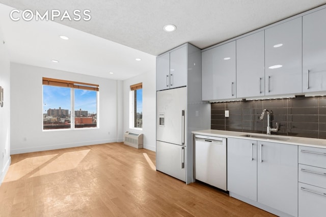 kitchen with white dishwasher, a sink, light countertops, light wood-style floors, and built in fridge