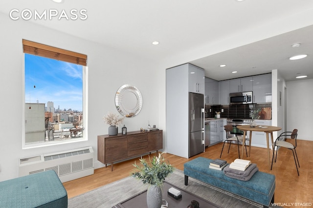 living room featuring radiator heating unit, light wood-style floors, and recessed lighting