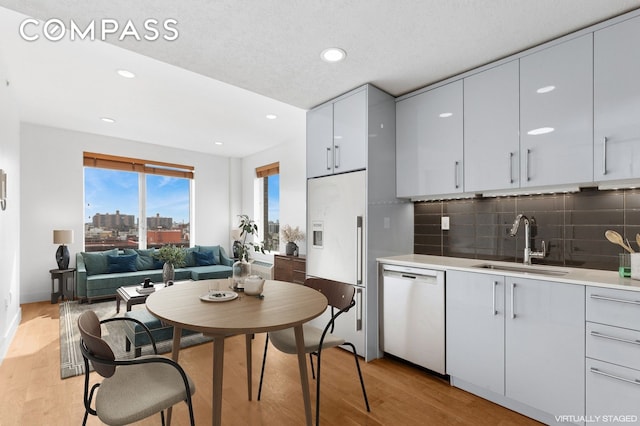 kitchen with light wood-style flooring, a sink, backsplash, white appliances, and light countertops