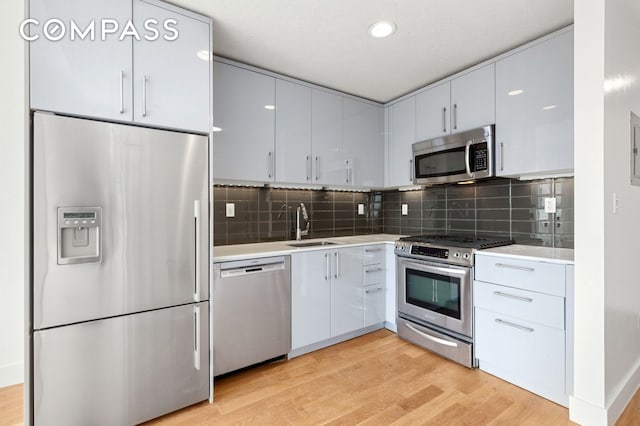 kitchen featuring stainless steel appliances, light countertops, light wood-style floors, and a sink