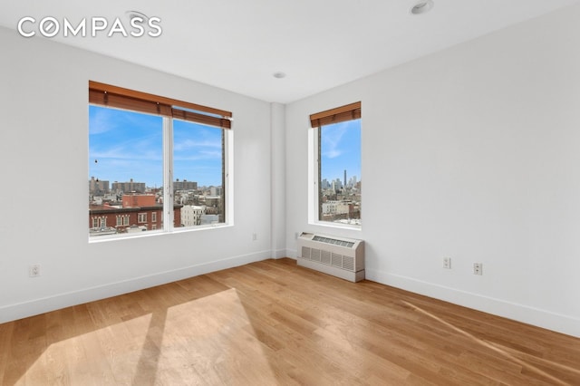 spare room featuring a view of city, wood finished floors, a wall unit AC, and baseboards