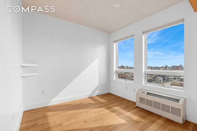 unfurnished room with radiator, baseboards, a city view, wood finished floors, and a textured ceiling