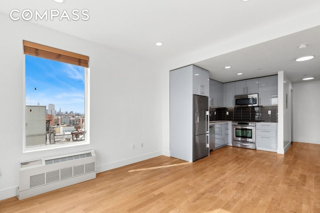 kitchen featuring radiator heating unit, tasteful backsplash, light wood-type flooring, stainless steel appliances, and baseboards