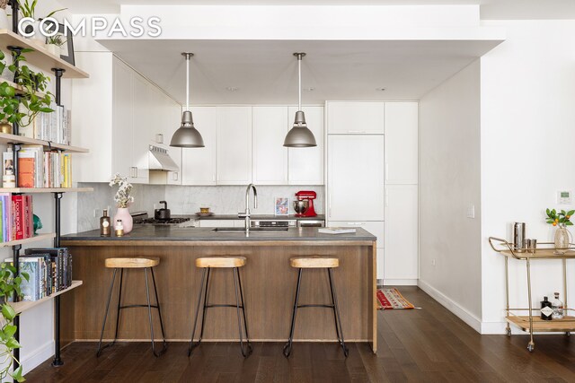 kitchen featuring under cabinet range hood, a peninsula, a sink, open shelves, and tasteful backsplash