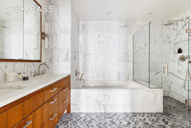 full bath with a sink, tile walls, a marble finish shower, a bath, and double vanity