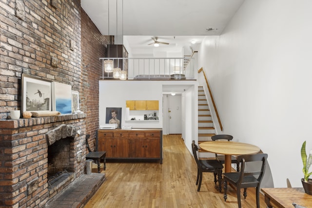 living area with a fireplace, light wood finished floors, a towering ceiling, ceiling fan, and stairs