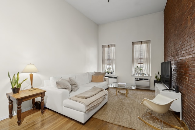 living room featuring brick wall, a high ceiling, wood finished floors, baseboards, and a brick fireplace