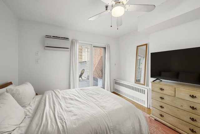 bedroom featuring wood finished floors, a ceiling fan, access to exterior, a wall mounted AC, and radiator heating unit