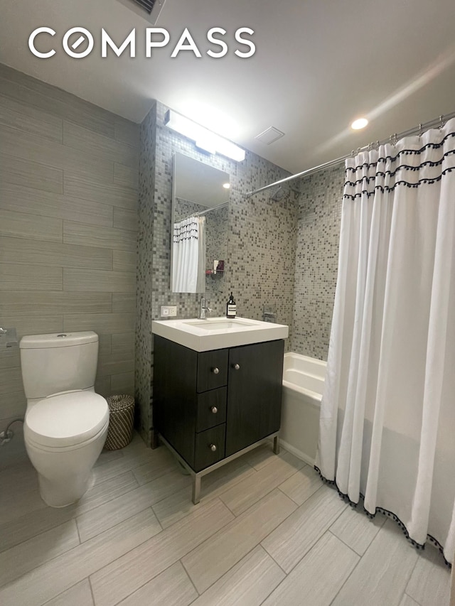 full bathroom with shower / bath combination with curtain, tile walls, toilet, and vanity