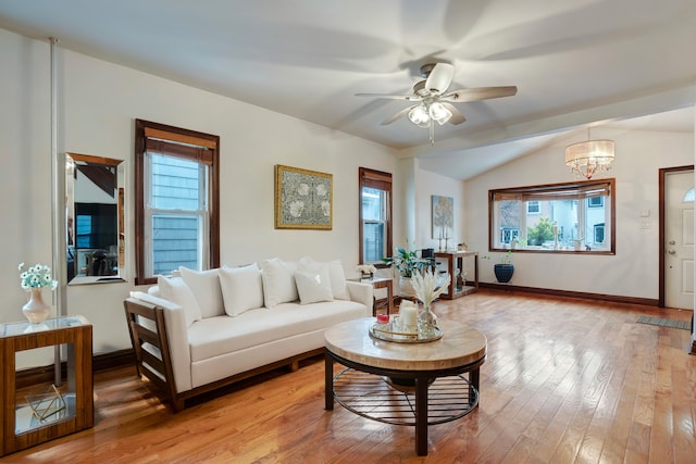 living room featuring vaulted ceiling, ceiling fan with notable chandelier, light wood-style flooring, and baseboards