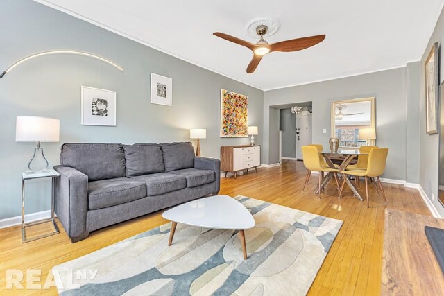 living area featuring a ceiling fan, baseboards, ornamental molding, and wood finished floors