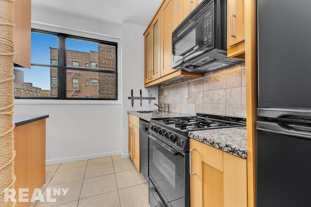 kitchen with light tile patterned floors, baseboards, backsplash, light stone countertops, and black appliances