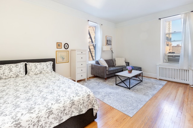 bedroom with light wood-style floors, radiator heating unit, multiple windows, and ornamental molding