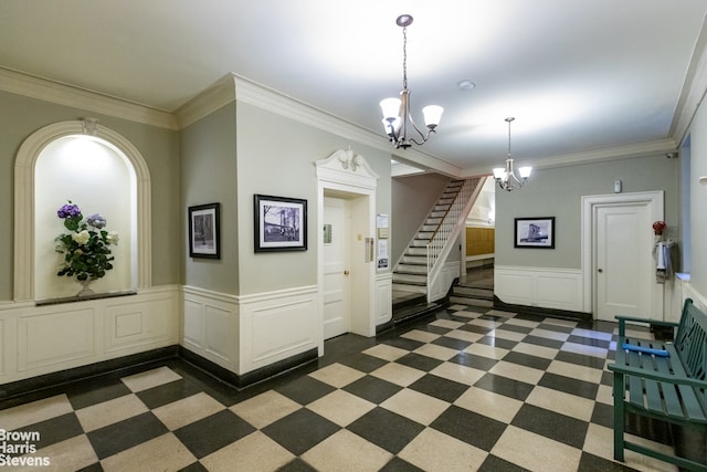 foyer entrance with ornamental molding, wainscoting, a notable chandelier, and stairs