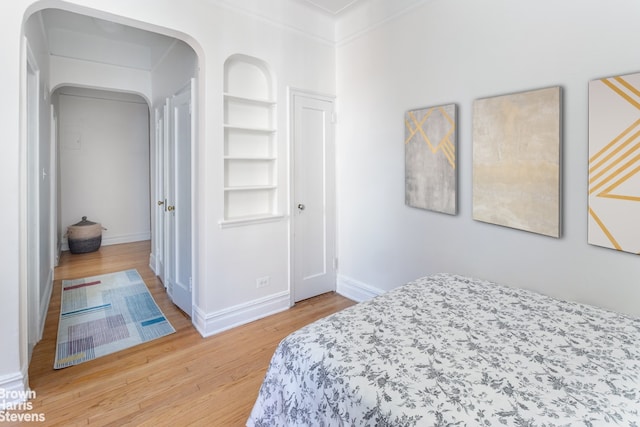 bedroom featuring crown molding, light wood-style flooring, and baseboards