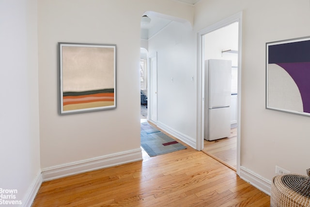 hall featuring light wood-style floors, arched walkways, and baseboards