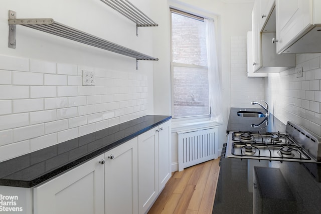 kitchen featuring light wood-type flooring, radiator heating unit, white cabinets, and backsplash