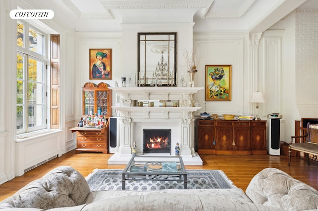 living area with crown molding, a decorative wall, a lit fireplace, and wood finished floors