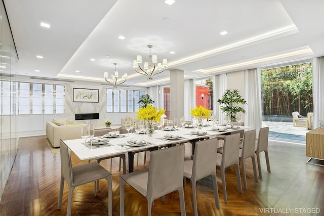 dining space featuring a chandelier, a premium fireplace, a raised ceiling, and recessed lighting