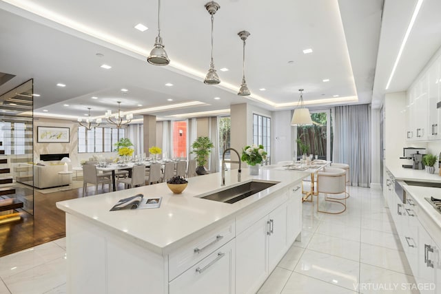 kitchen with a sink, light countertops, an island with sink, and a raised ceiling