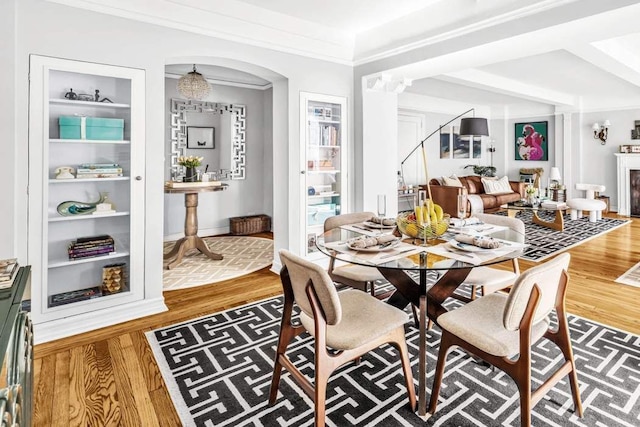 dining space with arched walkways, a fireplace, wood finished floors, built in features, and ornamental molding