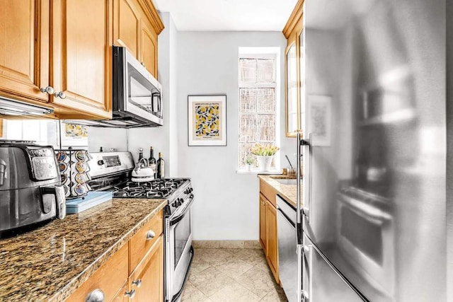 kitchen featuring appliances with stainless steel finishes, baseboards, and dark stone countertops