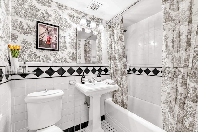 bathroom with a wainscoted wall, tile walls, visible vents, toilet, and wallpapered walls