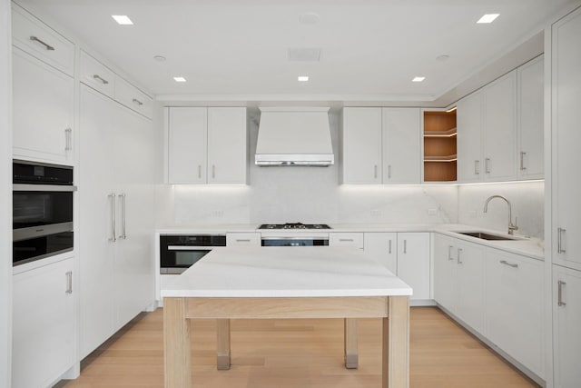 kitchen with oven, open shelves, custom exhaust hood, and a sink