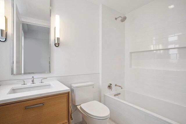 bathroom featuring a wainscoted wall, toilet, vanity, tile walls, and tiled shower / bath