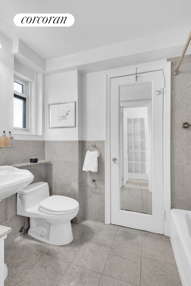 full bathroom featuring tile walls, wainscoting, toilet, and a tub to relax in