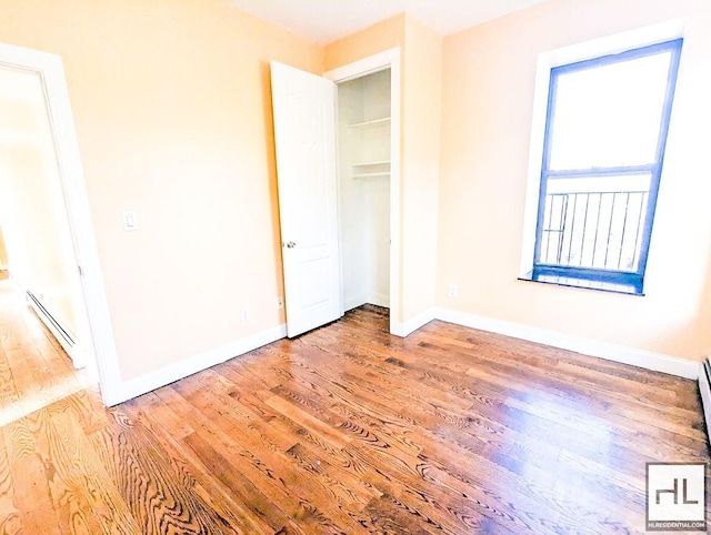 unfurnished bedroom featuring a closet, wood finished floors, baseboards, and baseboard heating