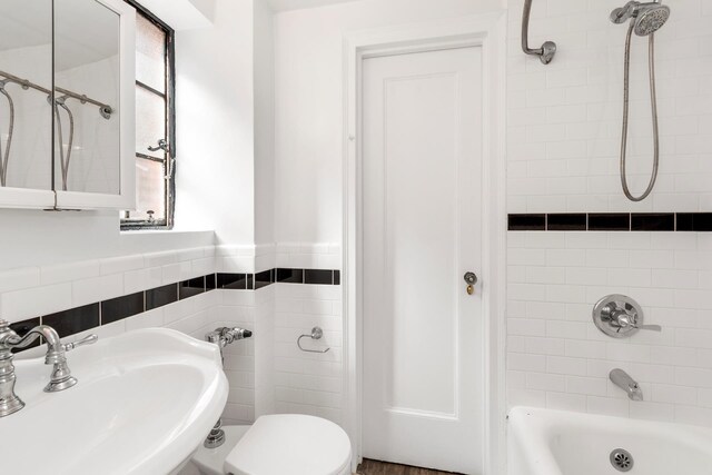 full bathroom featuring a sink, shower / washtub combination, toilet, tile walls, and a wainscoted wall