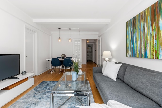 living area with beam ceiling, baseboards, and wood finished floors