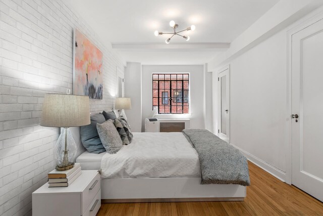 bedroom with light wood finished floors and brick wall