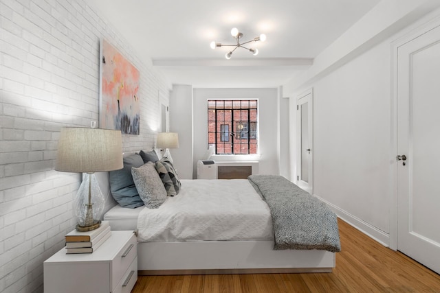 bedroom with brick wall, baseboards, beamed ceiling, and light wood finished floors